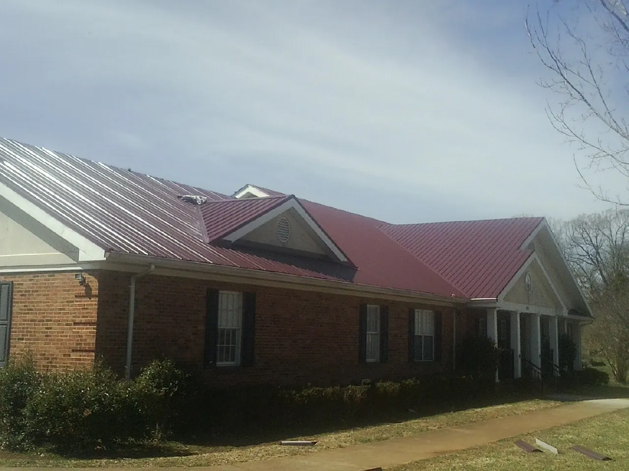 Red metal roof with gabled entries on a long brick building, from a Hail Damage Roof Repair job in Enfield