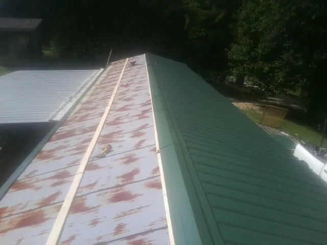 Old rusted panels beside newly installed green metal roofing — Wind Damage Roof Repair by Roofing Brothers in Enfield