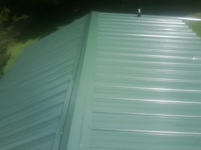 New green metal panels meeting at the ridge of a roof — Flat Roof Repair work by our crew in Enfield